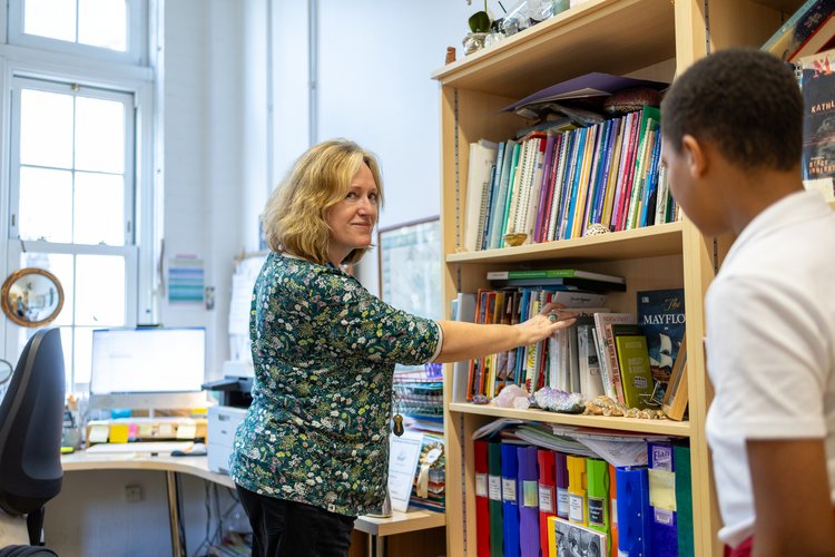 Teacher and pupil choosing a book from the library shelves, photographed from the side at Mayflower Primary School