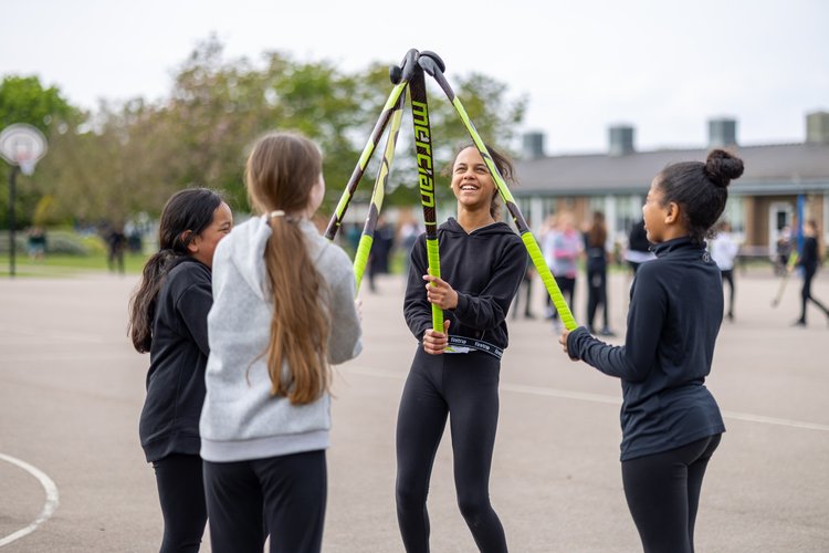 Girls with hockey sticks on the playground, photographed over the shoulder at Parsonage Farm Primary School